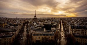 Picture of the city of Paris from the Arc de Triomphe showing the Eiffel Tower and two main streets with the sunset in the background.