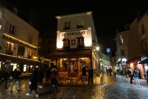 Picture of Le Consulat restaurant and two side streets with Christmas lights at night in the Montmarte neighborhood of Paris, France.