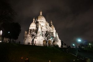 Picture of a lit-up Sacre Coeur Basilica and steps on a cloudy evening in Paris France.