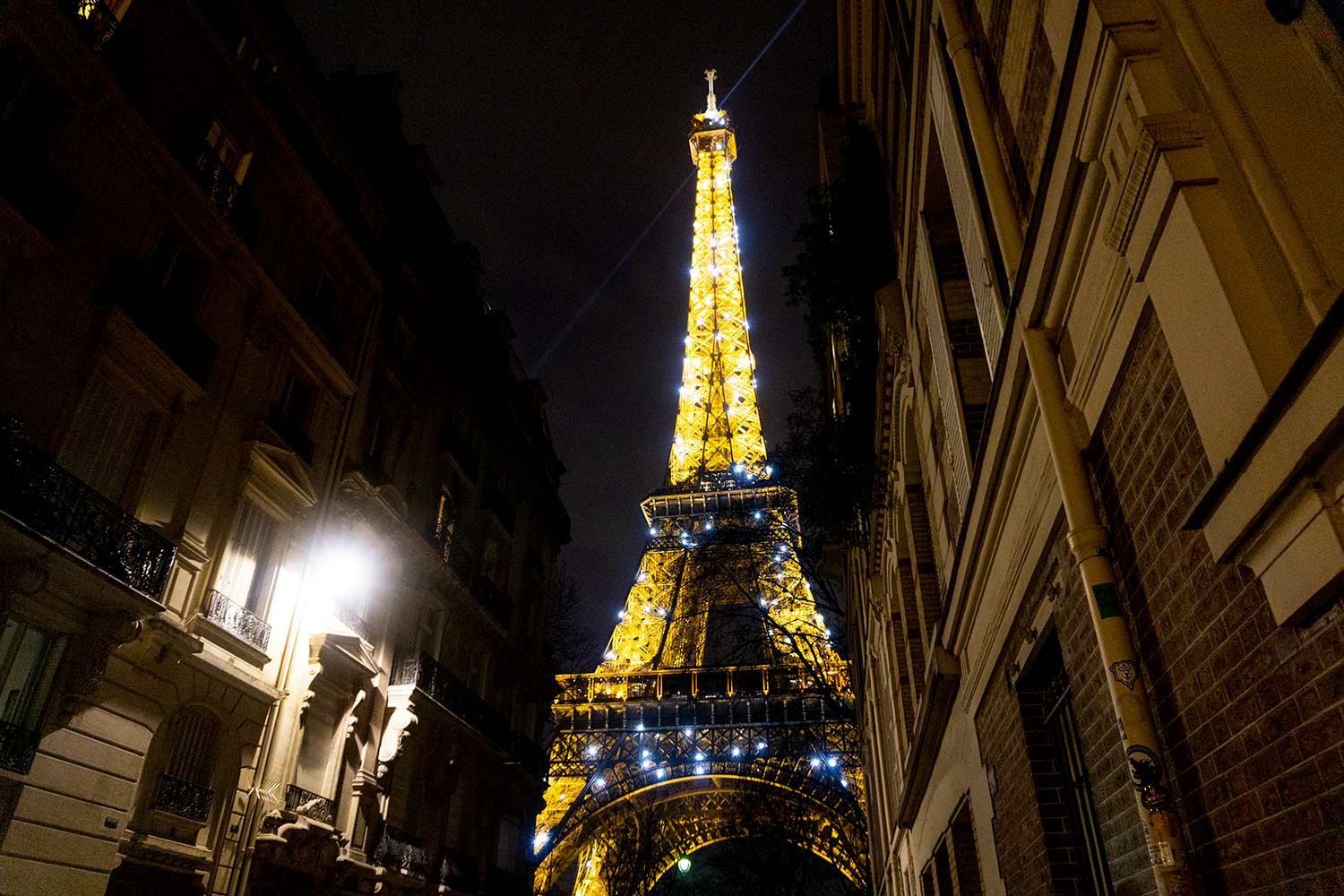 Night picture of the twinkling Eiffel Tower from a side street in Paris, France.
