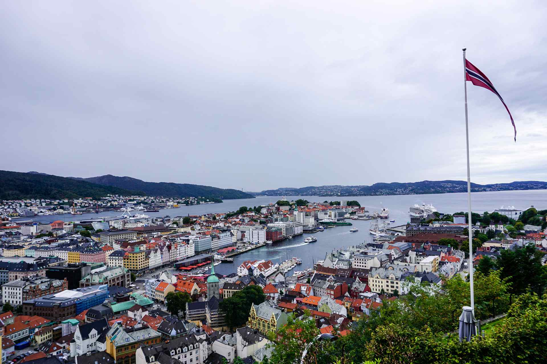 A picture of the Norwegian flag with the Bergen Harbor and buildings in the background.