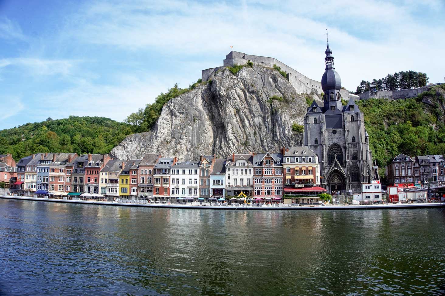 The village of Dinant, Belguim located on a river with a rock behind it.