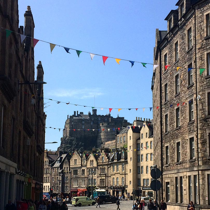 View of Edinburgh Castle from the Grassmarket with flags draped across the street.