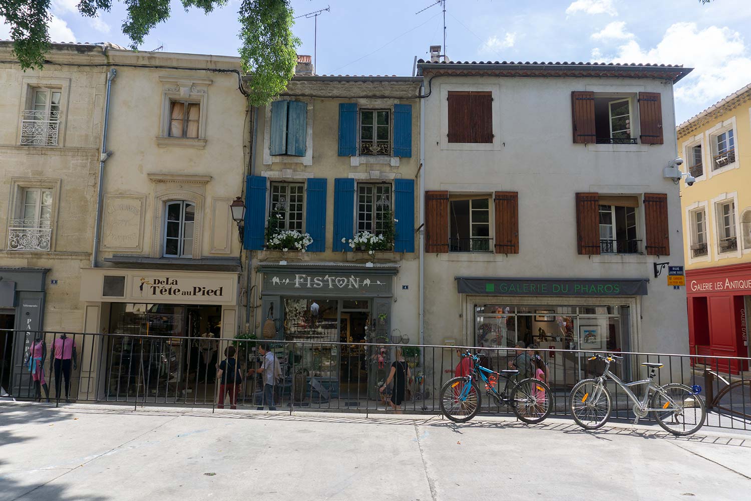 A plaza in Saint-Remy surrounded by buildings with colorful shutters. Two bikes are resting against a railing.