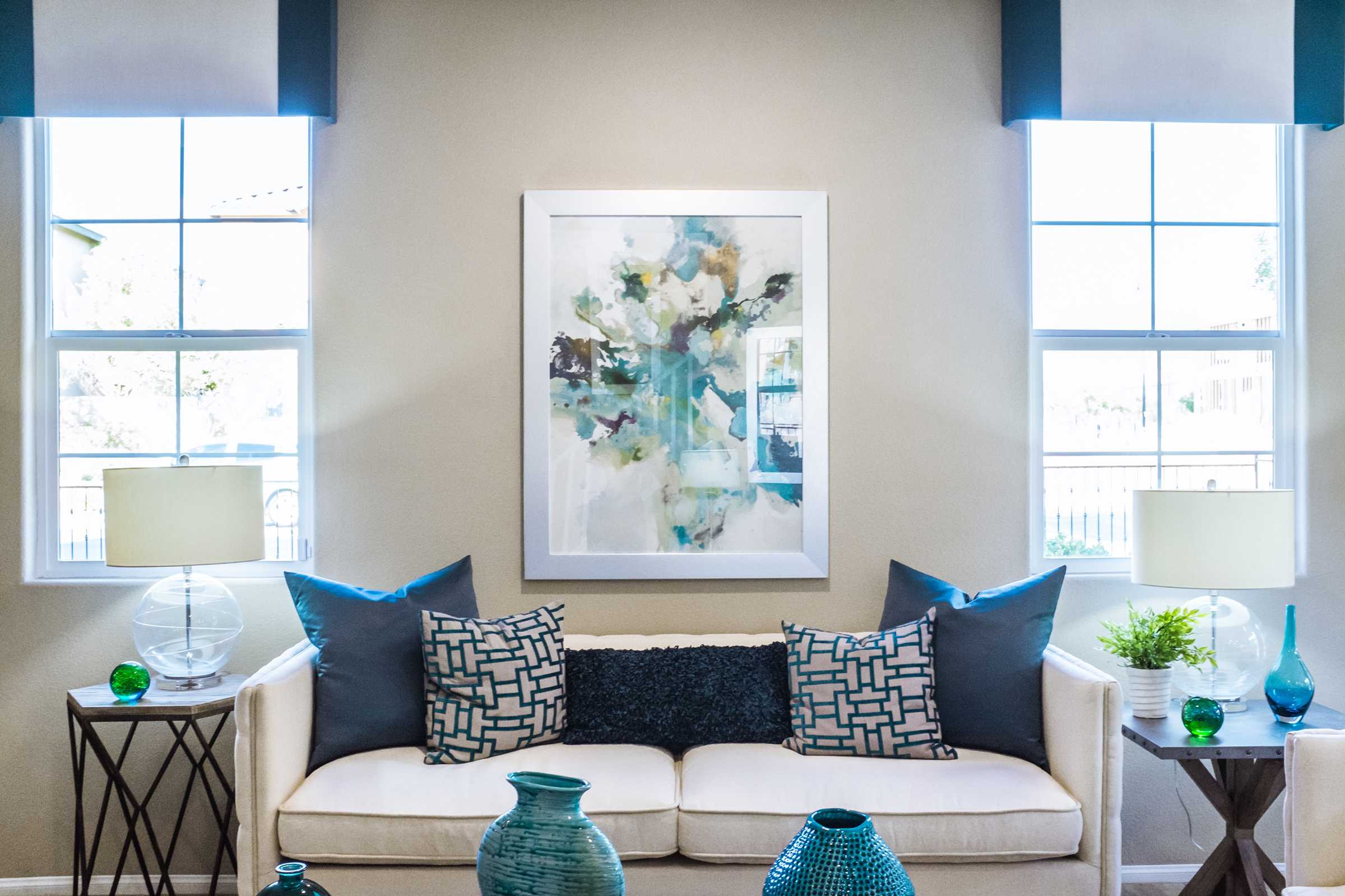 A white couch with blue pillows, two tables and a picture frame on the wall.