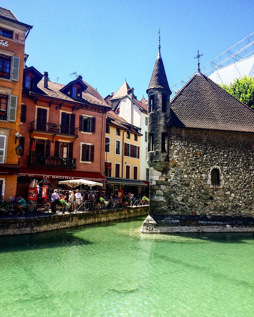 A stone building in the middle of canal with colorful buildings on the left side.