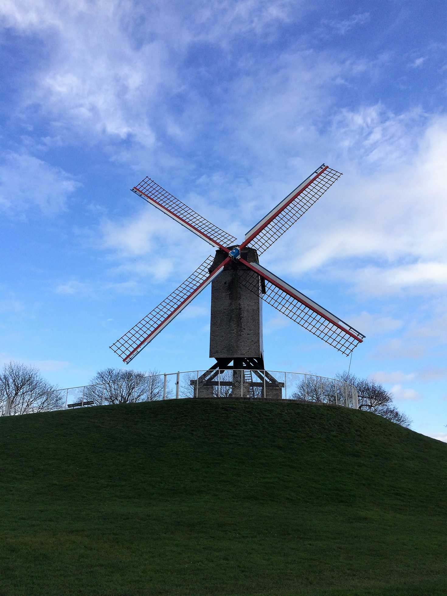 A picture of a windmill with a blue sky and green grass in Bruges, Belgium.
