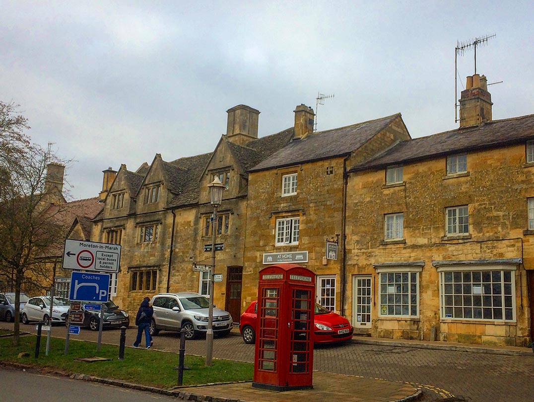 Stone buildings and a red telephone booth in the Cotswolds, England.