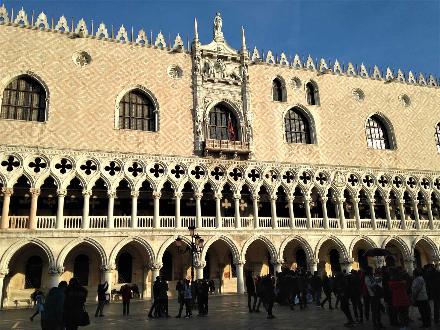 The ornate facade of the Doge's palace in Venice, Italy with a crowd of people standing outside.