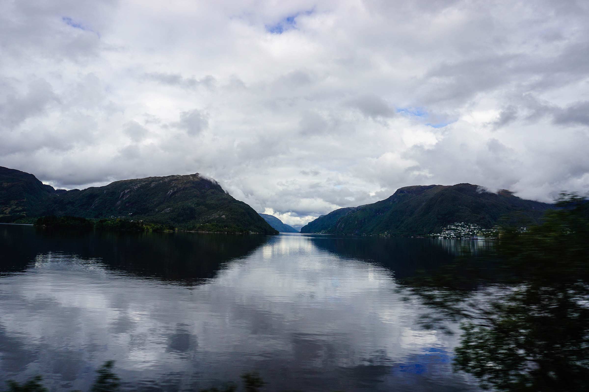 A picture of water in a fjord with mountains in the background and the reflection in the water.