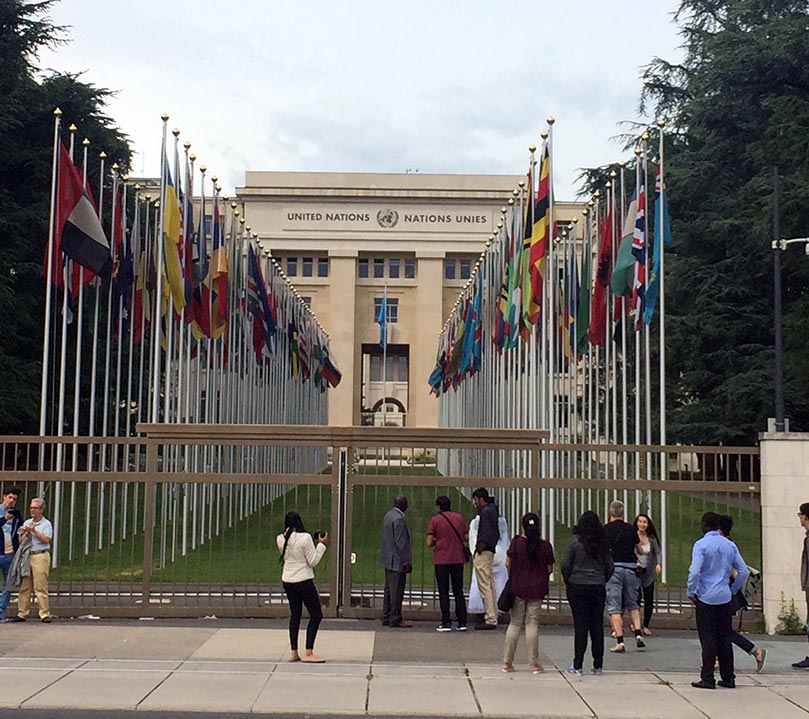 The outside of the UN building in Geneva, Switzerland with the flags of all the countries in a row outside of the entrance.