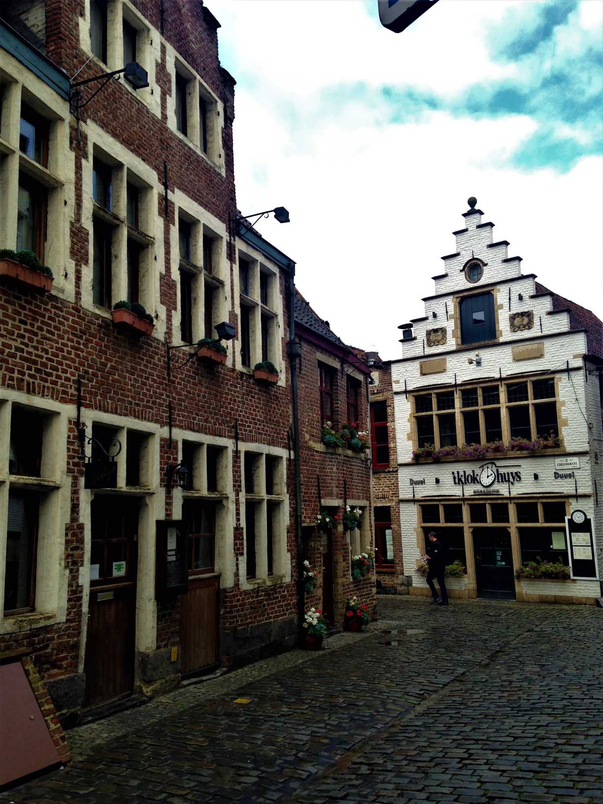 This picture shows a street in Ghent, Belgium with a brick building to the left and a white brick building with gables in the background.