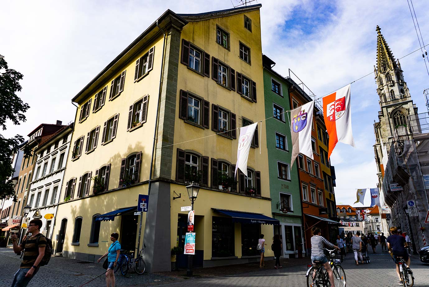 A street in Konstanz, Germany with medieval banners hanging and bicyclists below.