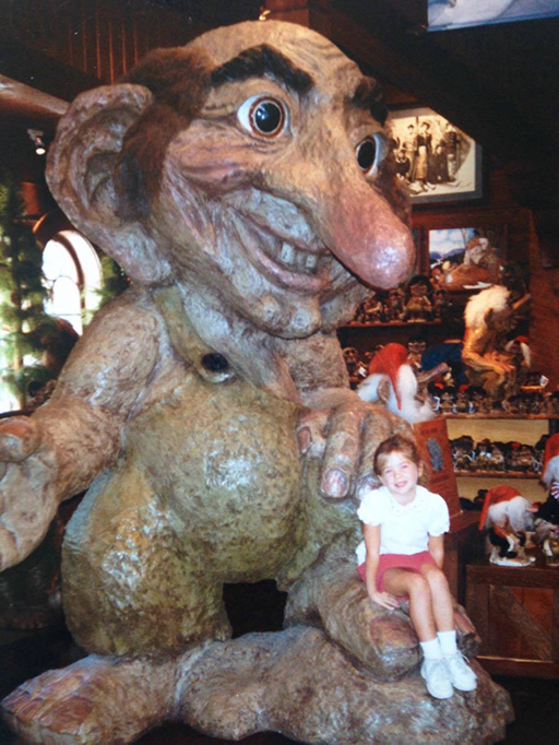 A picture of a child sitting on the foot of a large wooden troll at Walt Disney World.
