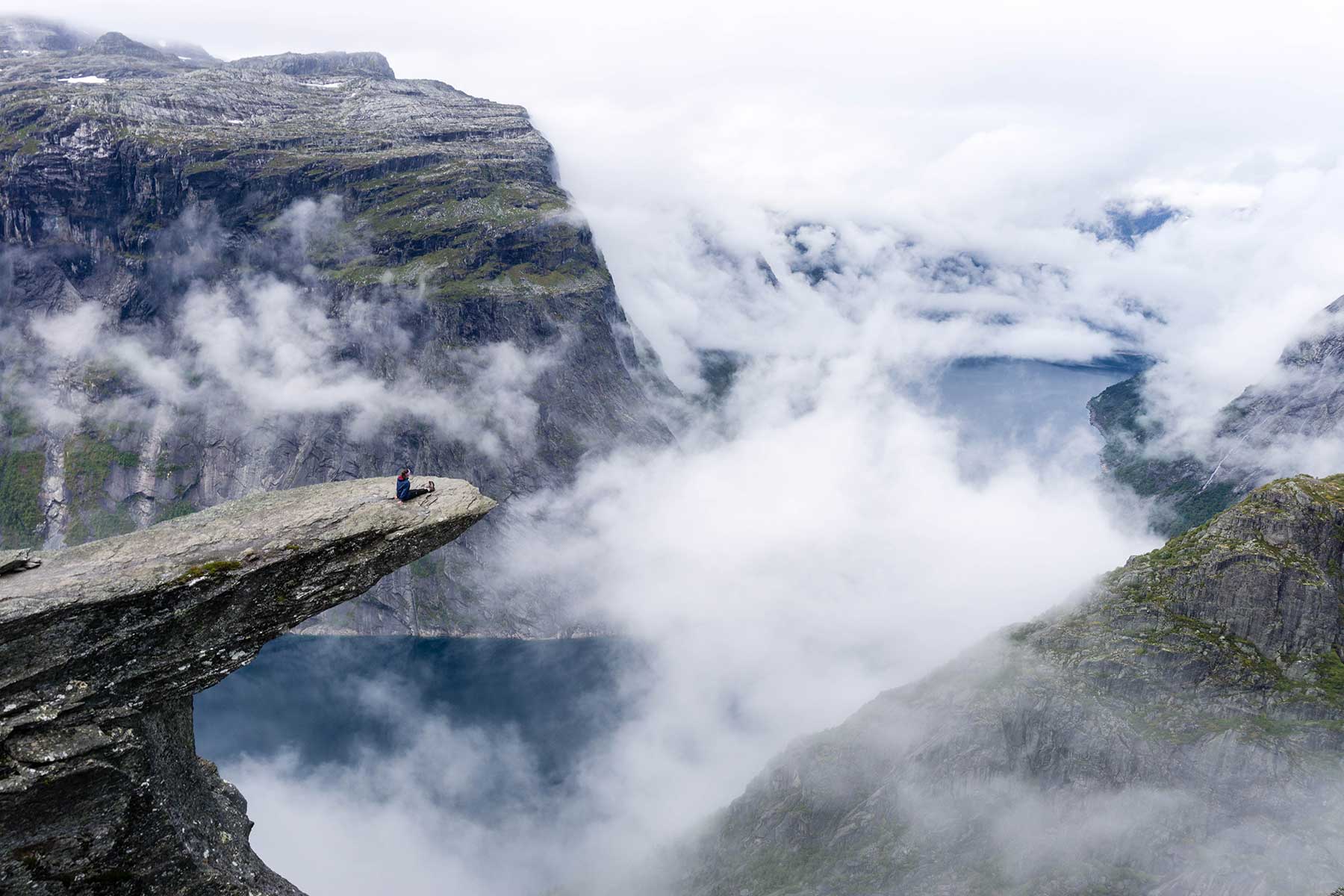 A picture of a girl sitting near the edge of Trolltunga, a rock jutting over the edge of a fjord, in Norway.
