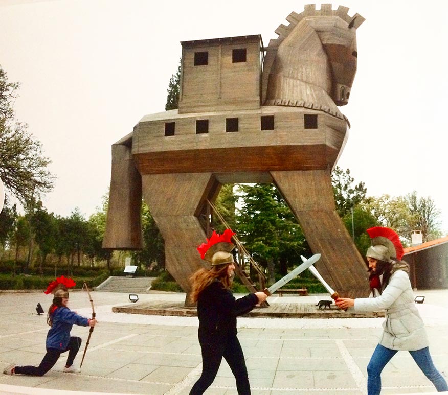 Three girls pretending to sword fight, and using a bow and arrow in front of the Trojan horse in Troy.