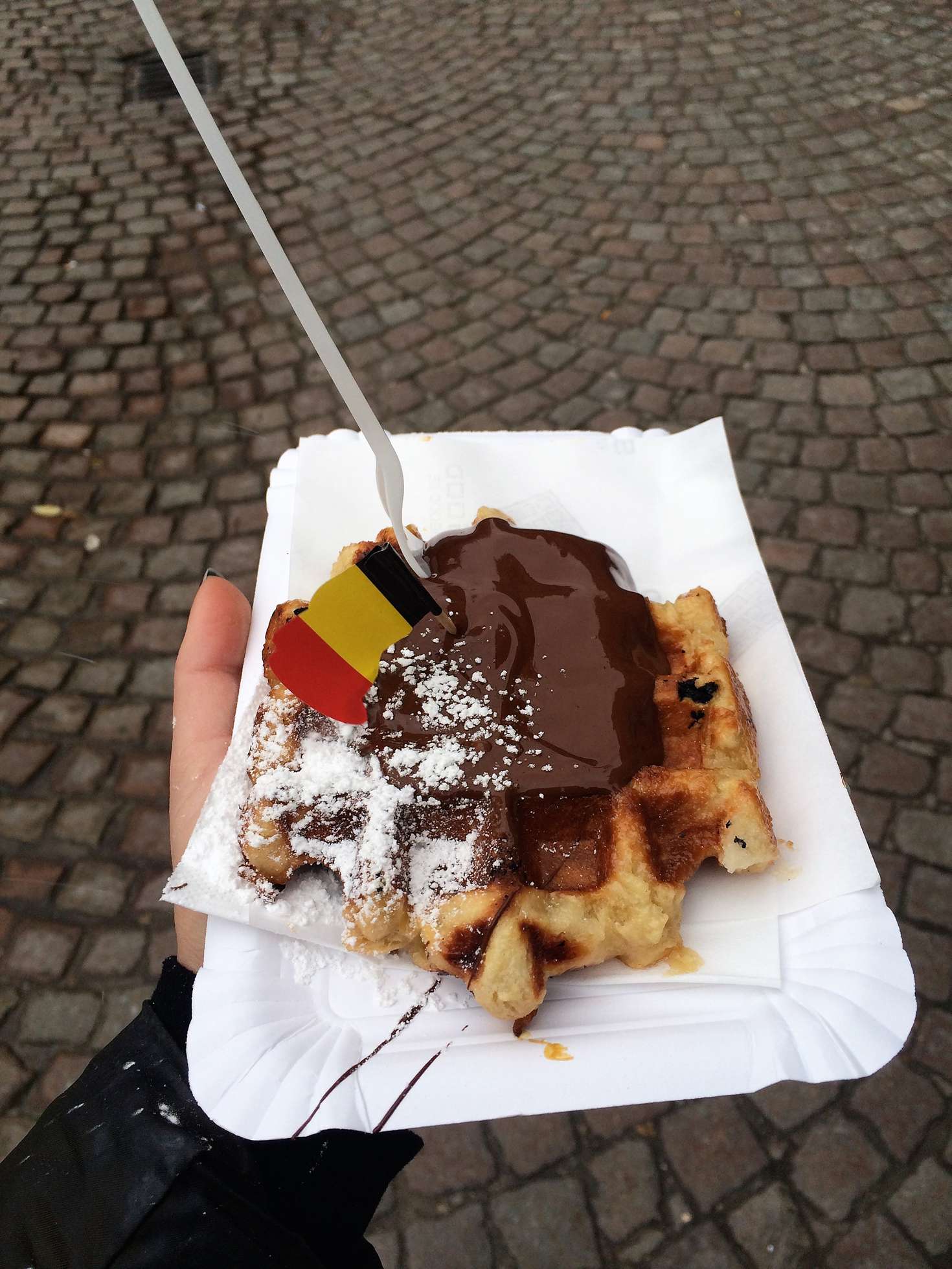 A picture of a liege waffle covered in nutella and topped with powdered sugar and a Belgian flag in Bruges, Belgium.