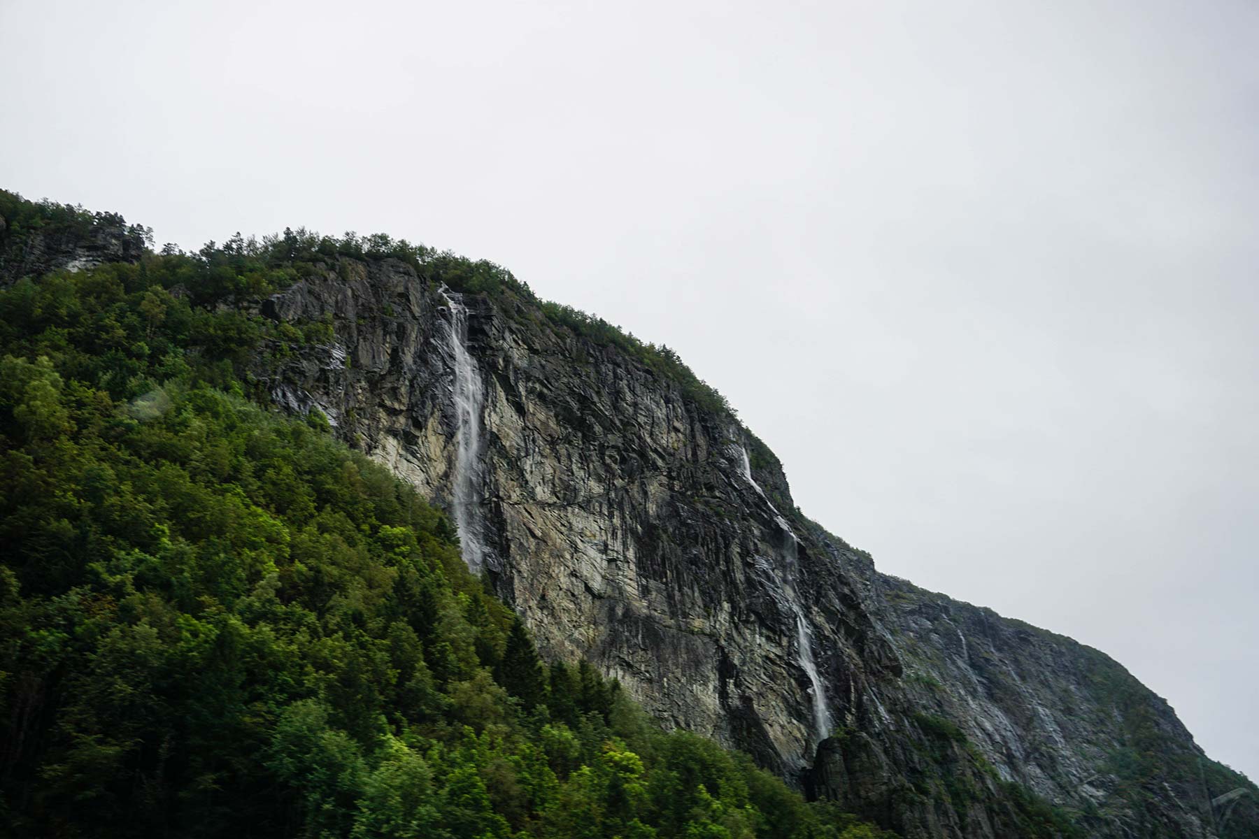 A picture of a cliff surrounding a fjord with a waterfall flowing from the top.