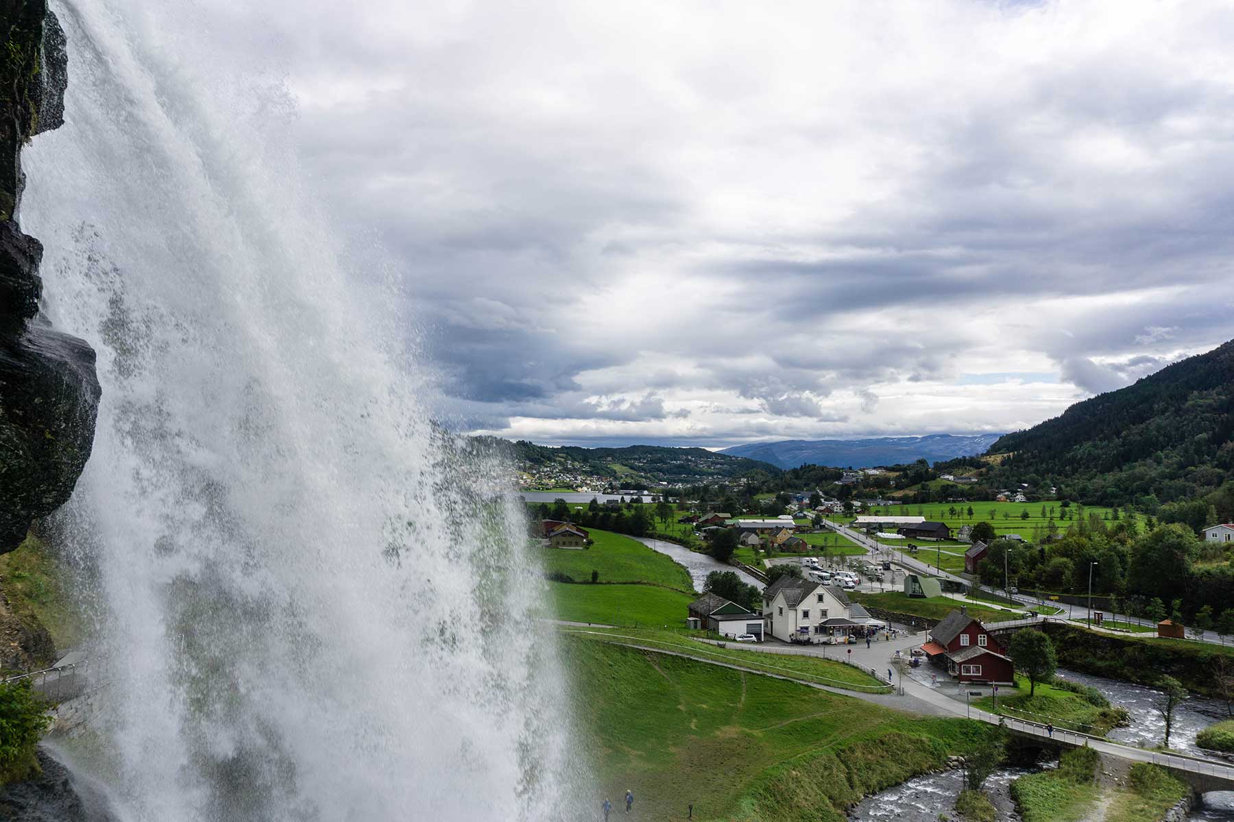 Picture of a waterfall in Norway with a green valley and mountains in the background.