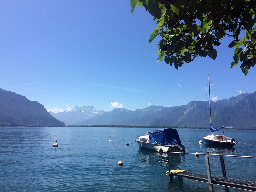 Boats in the water of Lake Geneva with mountains in the backgound.